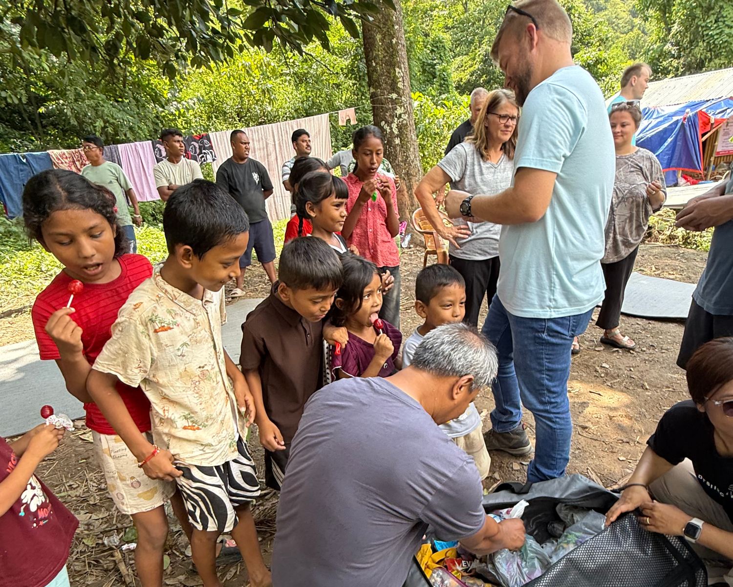 Children holding lollipops watch as a man unpacks a bag.